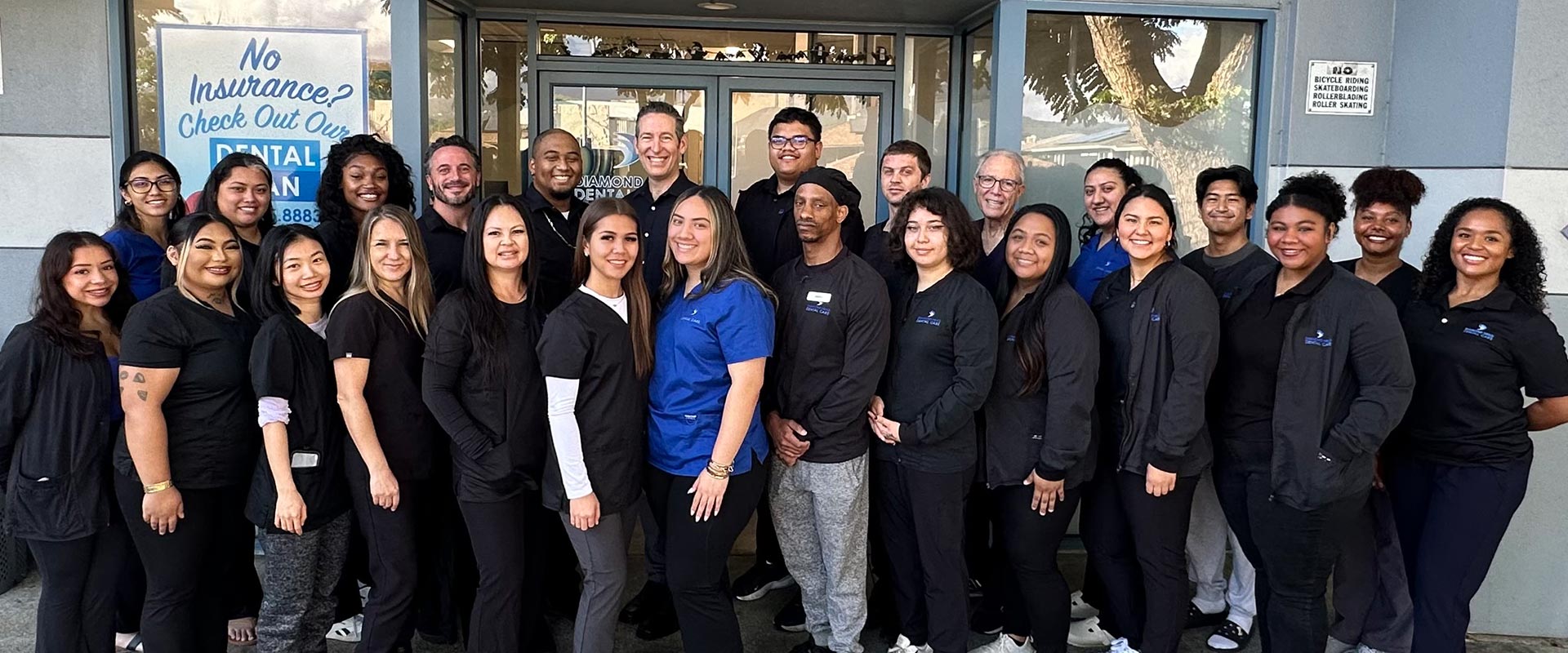 The image shows a group of people standing together outdoors, likely posing for a photograph, with a sign behind them that reads No Entry, indicating they are outside a restricted area.